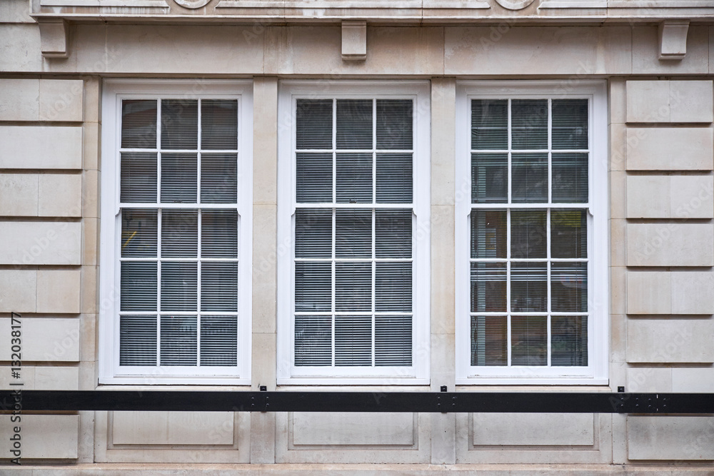 Window section with three colonial style windows in sand colored ashlar walling building facade Window section with three colonial style windows in sand colored ashlar walling building facade