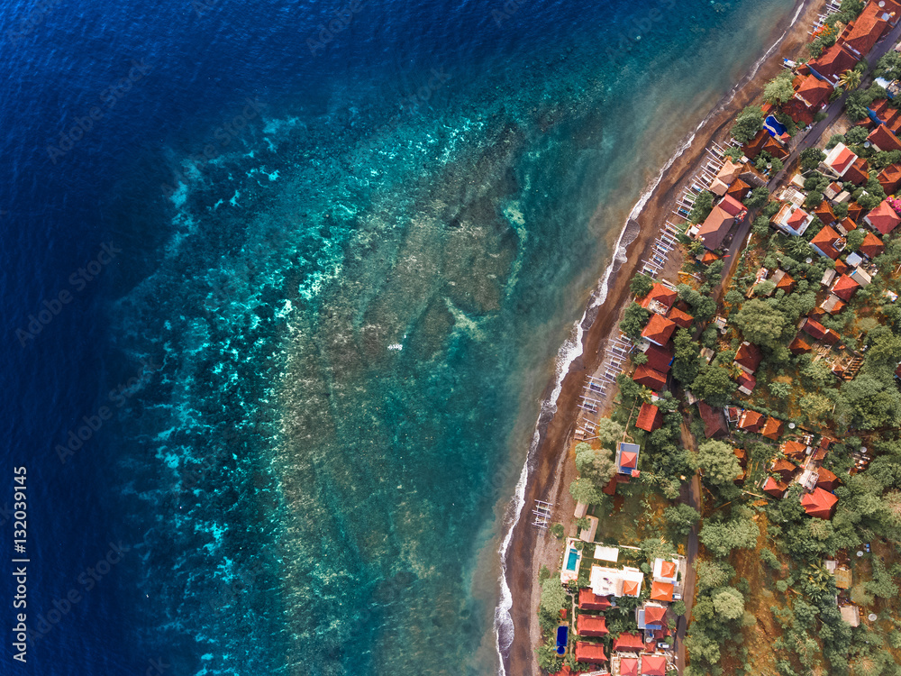 Aerial shot of underwater coral reef near shore with buildings. Bali, Indonesia