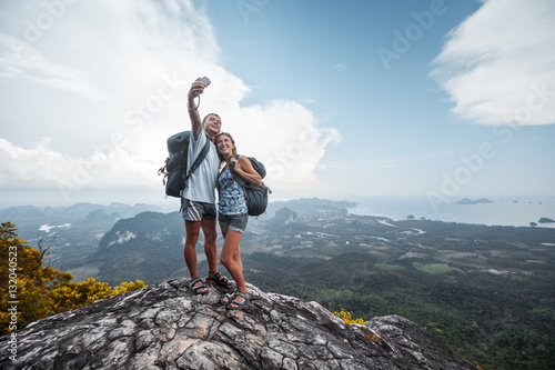 Couple of hikers taking selfie from top of the mountain with valley view on the background