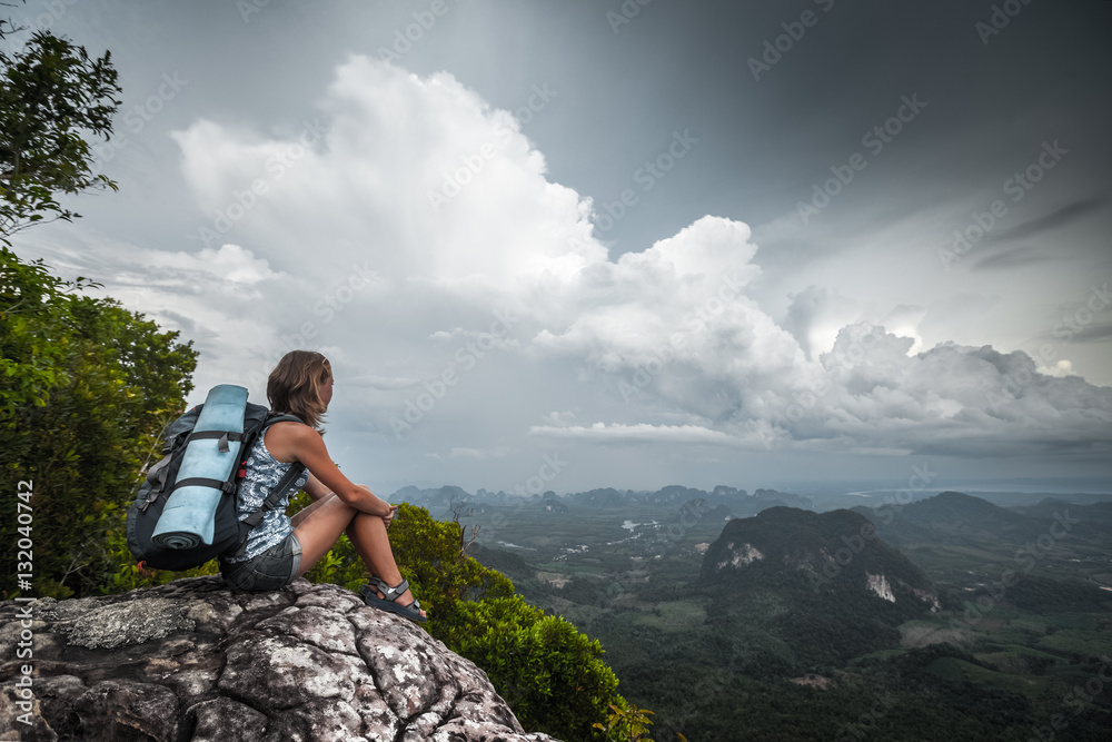 Young woman with backpack sitting on a cliff and enjoying a the view of valley