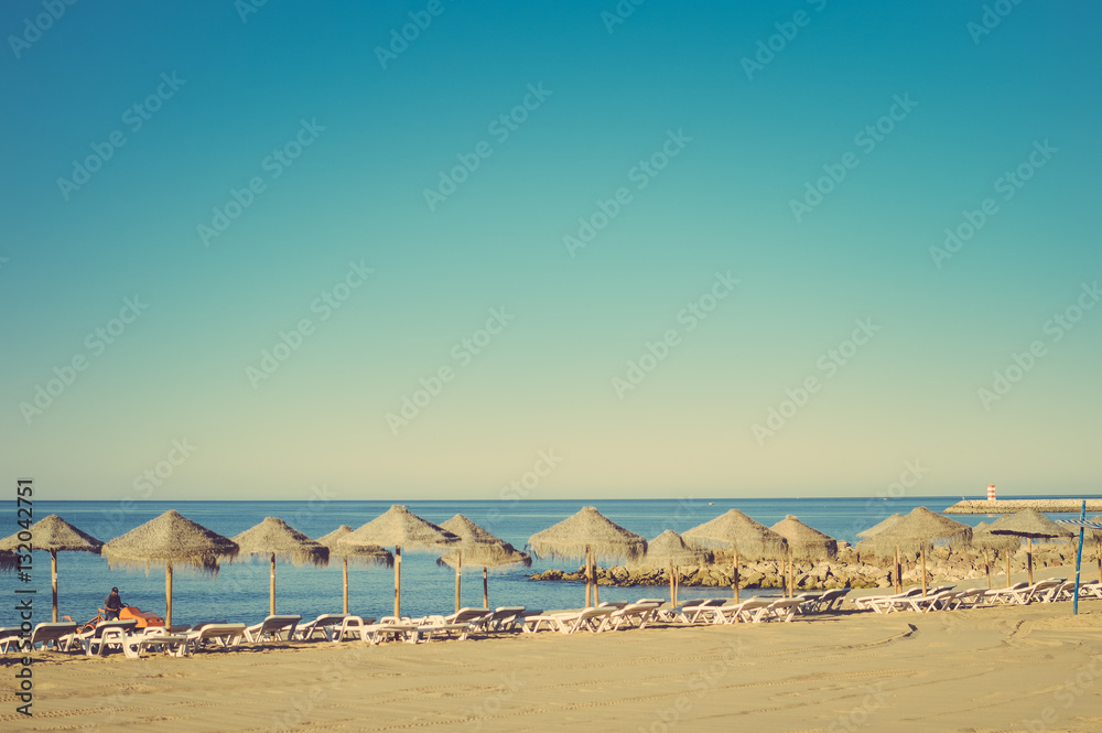 Holiday and vocation image with sandy beach, parasol and chairs on outdoors background