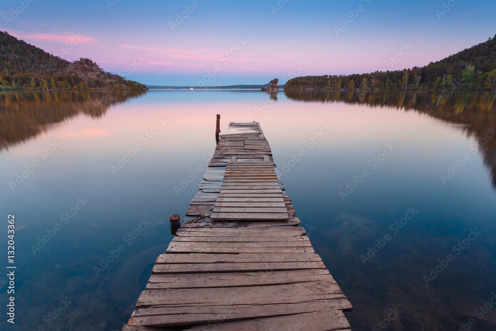 Fototapeta premium Wooden pier on a blue lake sunset and smooth reflection on water. Long exposure; Borovoye Lake; Kazakhstan.