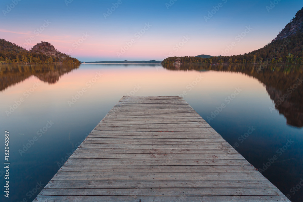 Wooden pier on a blue lake sunset and smooth reflection on water. Long exposure; Borovoye Lake; Kazakhstan. Wooden pier on a blue lake sunset and smooth reflection on water. Long exposure; Borovoye Lake; Kazakhstan.