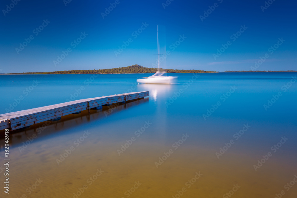 Blurred silhouette of white yacht moored to the lake pier. Long exposure shot.