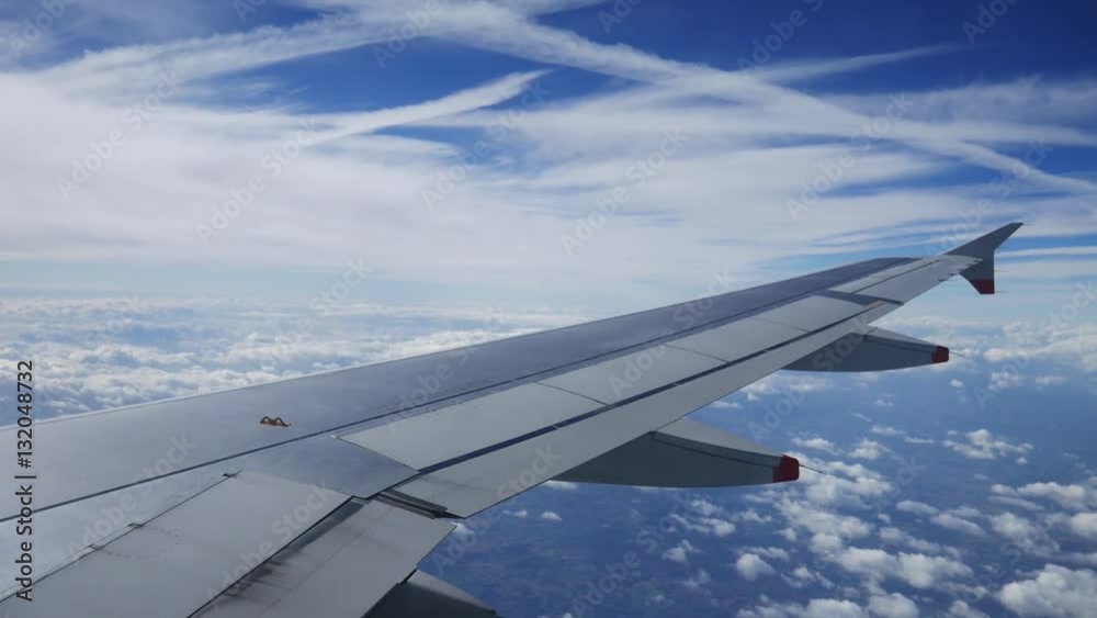 Wing of an airplane flying above the clouds with blue sky. View at the sky from the window of the plane.
Wing of an airplane flying above the clouds with blue sky. View at the sky from the window of the plane.