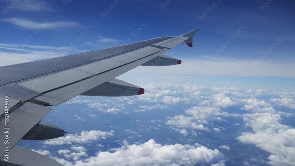 Wing of an airplane flying above the clouds with blue sky. View at the sky from the window of the plane.
Wing of an airplane flying above the clouds with blue sky. View at the sky from the window of the plane.