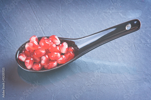 pomegranate seeds in a ceramic spoon and a sprig of rosemary on a dark surface