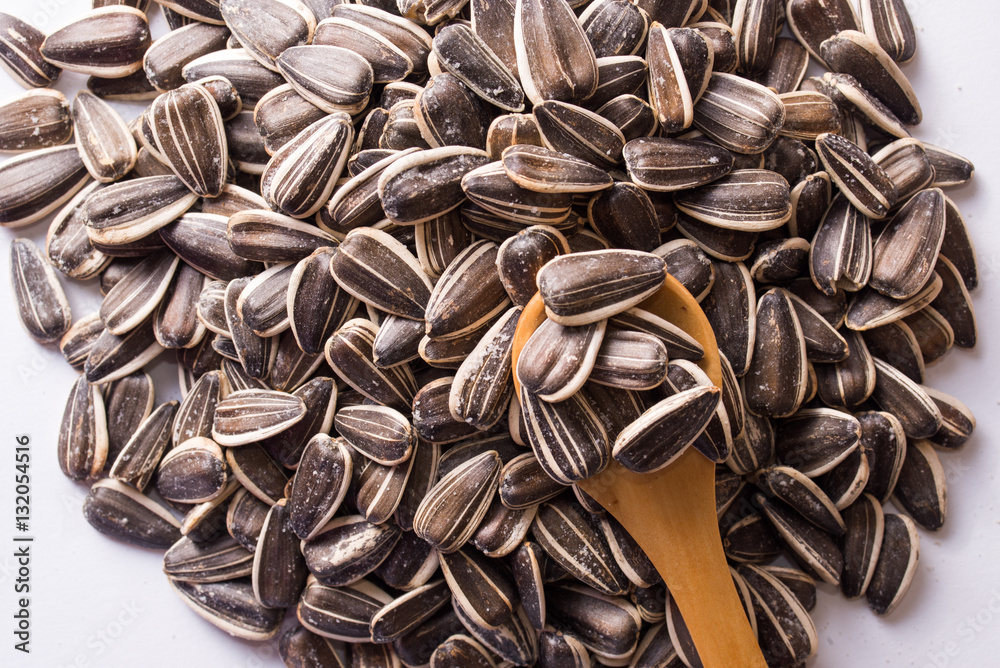 Sunflower seeds and a wooden spoon on a white background