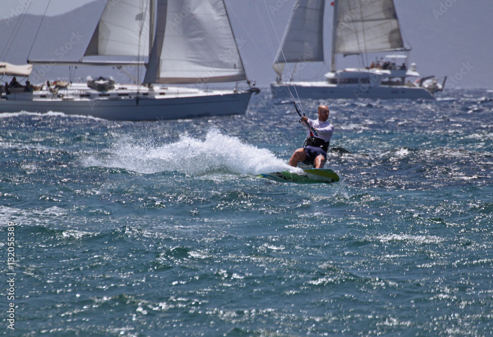 Naklejka premium young white male kitesurfing with sailboats behind in aegean sea 