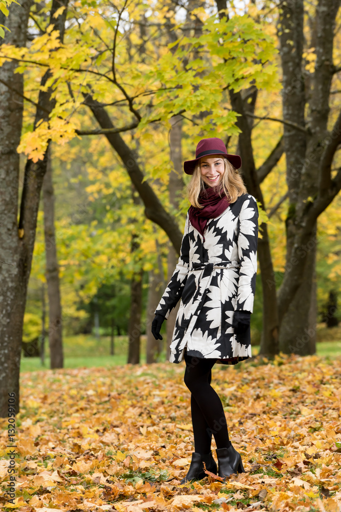 Woman in a floral patterned coat and wine red hat in the park. Happy girl and colorful autumn forest. Portrait of a lady, yellow, green, red and brown leaves background Woman in a floral patterned coat and wine red hat in the park. Happy girl and colorful autumn forest. Portrait of a lady, yellow, green, red and brown leaves background