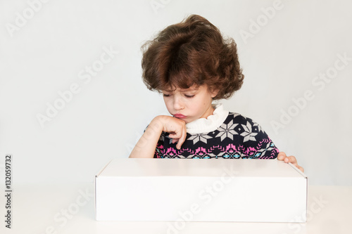 Surprised cute boy looking sad at a white box. The sweater with an ornament. White background.