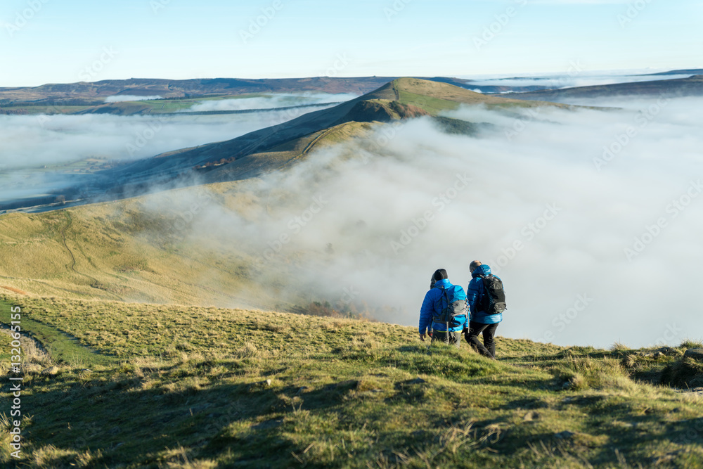 Male and female hikers walk along the great ridge along from Mam Tor, Peak District, Hope Valley on a cold winter morning