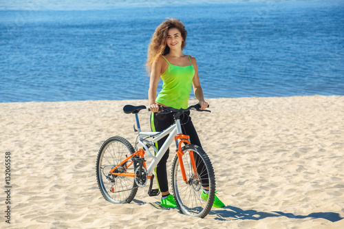Girl athlete with long curly hair wearing black sweat pants and a light green T-shirt to go with the bike in the morning on the shore near the ocean.