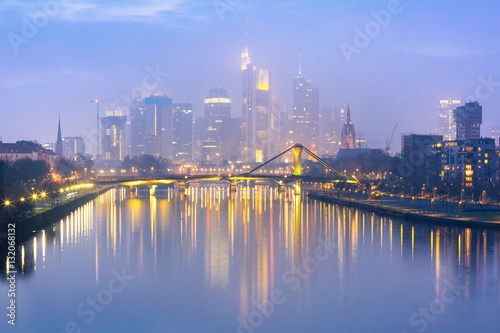 Picturesque view of foggy Frankfurt am Main skyline during evening blue hour with mirror reflections in the river, Germany