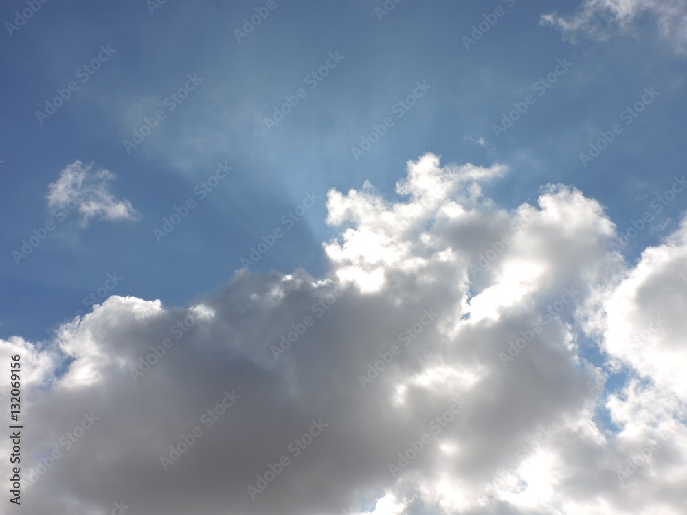 Fototapeta premium Sunshines coming from behind puffy clouds