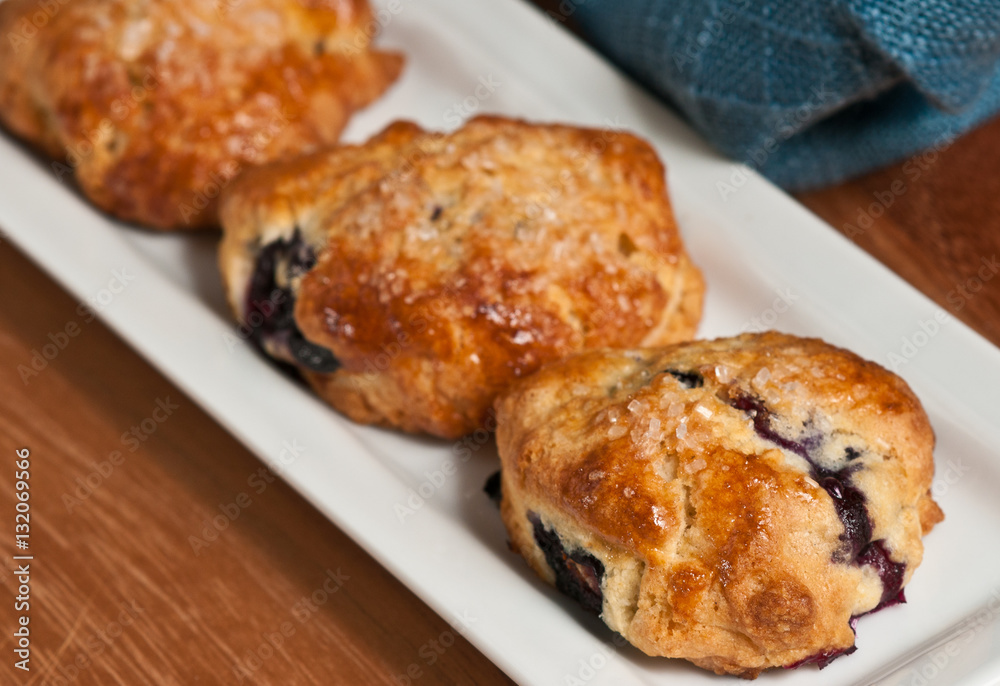 Blueberry filled scones on a white, rectangular plate on a wooden cutting board with a blue cloth napkin