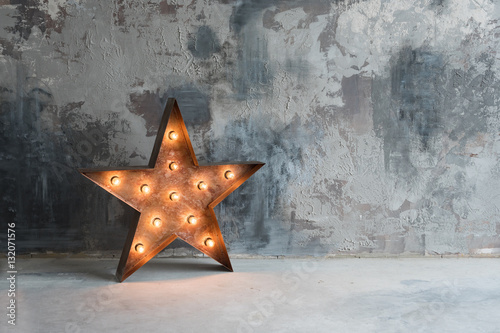 Large decorative retro star with lots of burning lights on grunge concrete background. Beautiful decor, modern design element. The loft style studio. Free space for text