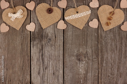 Top border of handmade burlap hearts with ribbon and buttons over a rustic wooden background