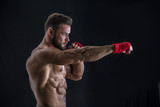 Young handsome topless boxer in red gloves looking at camera on black studio