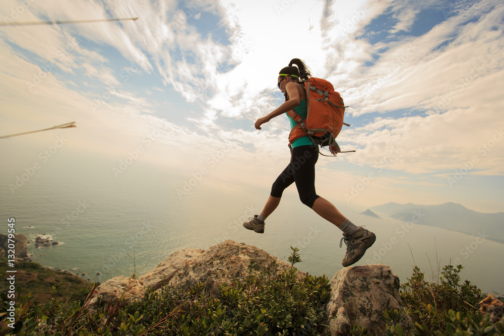 successful hiker jumping on seaside mountain peak rock