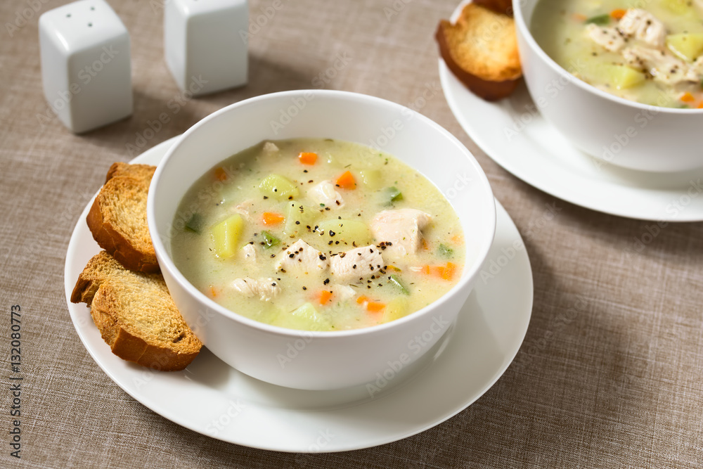 Chicken and potato chowder soup with green bell pepper and carrot in bowls with toasted bread slices on the side, photographed with natural light (Selective Focus, Focus one third into the first soup) Chicken and potato chowder soup with green bell pepper and carrot in bowls with toasted bread slices on the side, photographed with natural light (Selective Focus, Focus one third into the first soup)