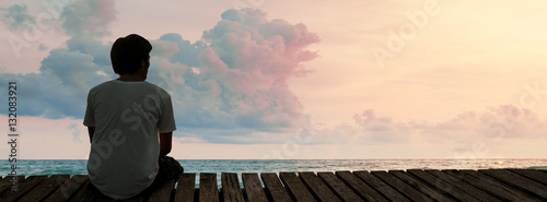 Lonely Man sitting in a wooden dock pier in sea beach with twilight sky