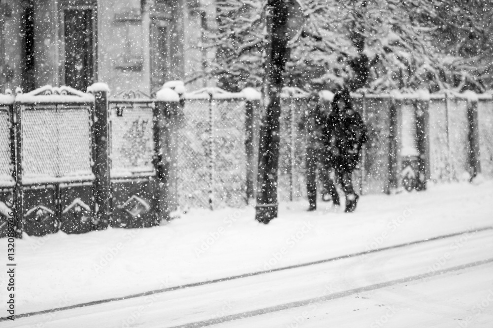 Snowing urban landscape with people passing by
