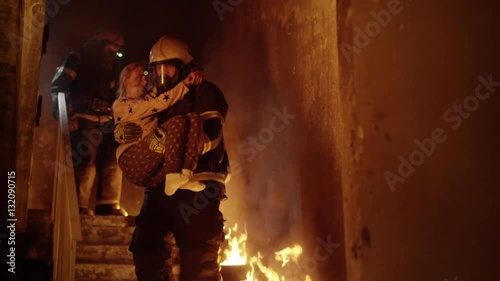 Burning Building. Group Of Firemen Descend on Burning Stairs. One Fireman Holds Saved Girl in His Arms.  Shot on RED EPIC (uhd). photo