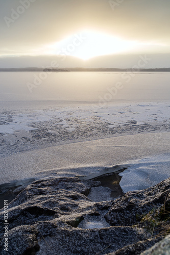 Snowy rock by a frozen and snowy lake in Finland at morning in the winter.