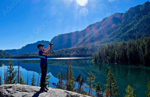 Hiking in Washington State in Pacific Northwest. Woman on cliff by tranquil lake with reflections of mountains.  Snow Lake.  Enchantment lakes basin. Leavenworth. Seattle. WA. United States. 