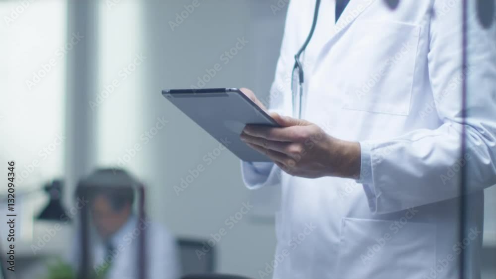 Senior Doctor Thinking About Diagnosis and Consulting Tablet Computer. His Office is Bright and Modern.  Shot on RED Cinema Camera in 4K (UHD).
