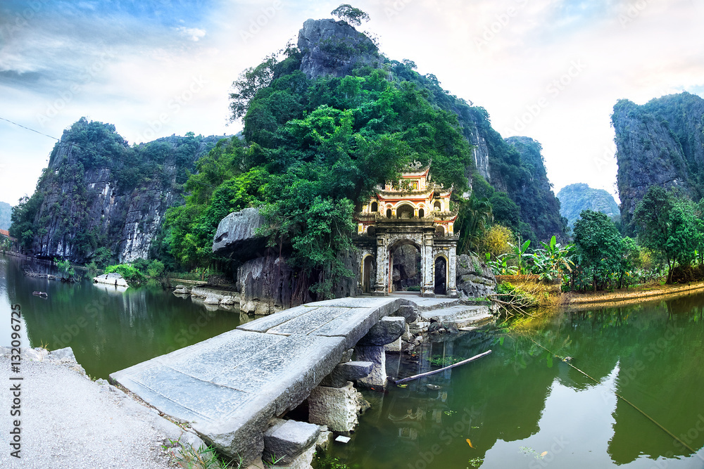 Outdoor park landscape with lake and stone bridge. Gate entrance to ancient Bich Dong pagoda complex. Ninh Binh, Vietnam travel destination.