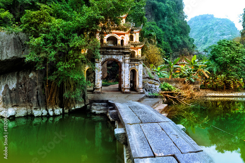 Outdoor park landscape with lake and stone bridge. Gate entrance to ancient Bich Dong pagoda complex. Ninh Binh, Vietnam travel destination. photo