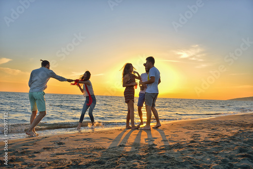 group of happy young people dancing at the beach on beautiful summer sunset