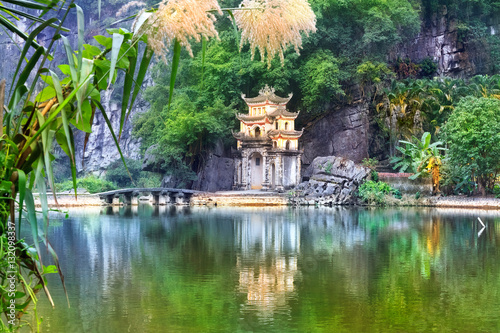 Outdoor park landscape with lake and stone bridge. Gate entrance to ancient Bich Dong pagoda complex. Ninh Binh, Vietnam travel destination. photo