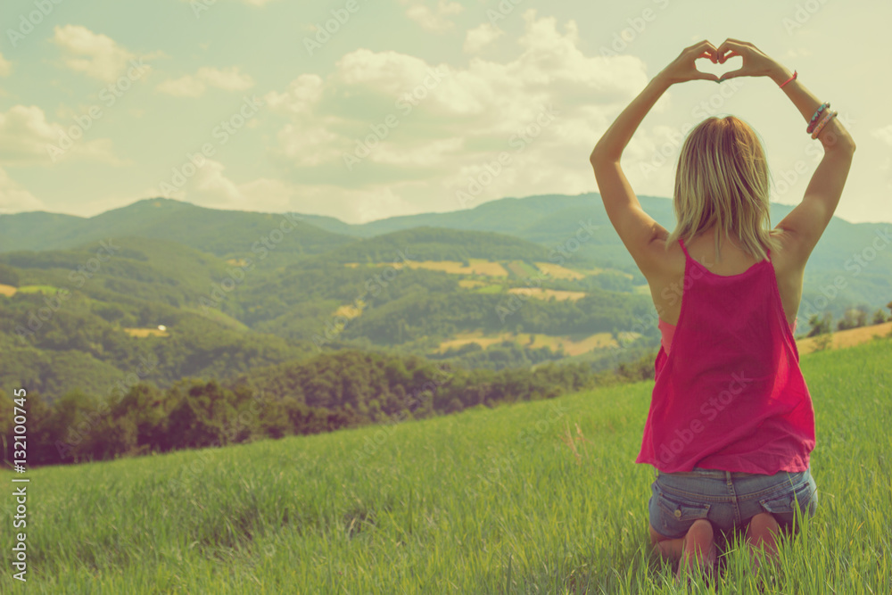 Girl making a heart-shape with her hands outdoors.