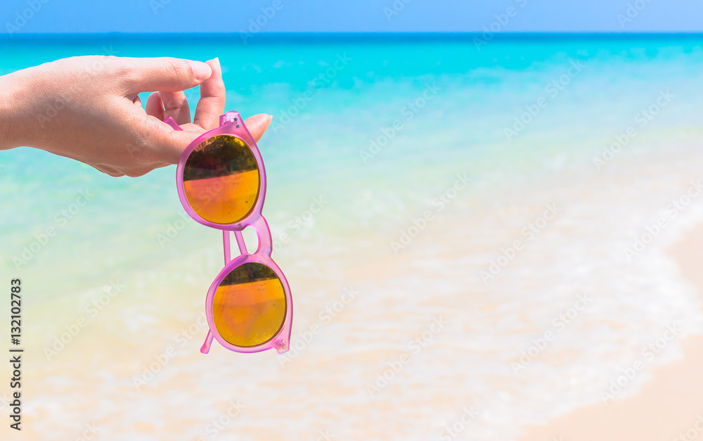 Woman hand hold sunglasses over sea background Woman hand hold sunglasses over sea background
