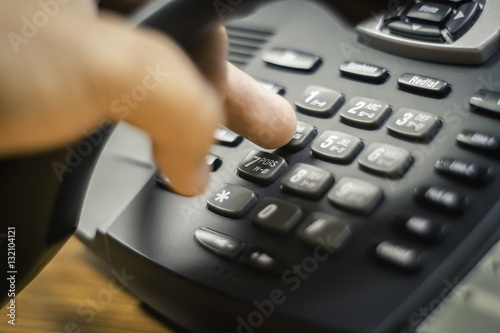 businessman dialing voip phone in the office, keyboard and monitor detail in the background with vintage color tone effect