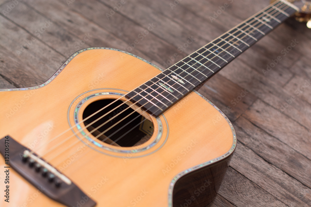 Obraz premium Acoustic guitar resting against a wooden background with copy sp