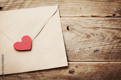 Envelope or letter and red heart on vintage wooden table for love message on Valentines Day in retro toning.