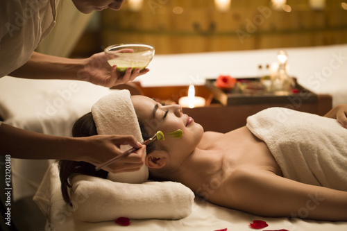 Young woman receiving facial treatment from masseuse in spa