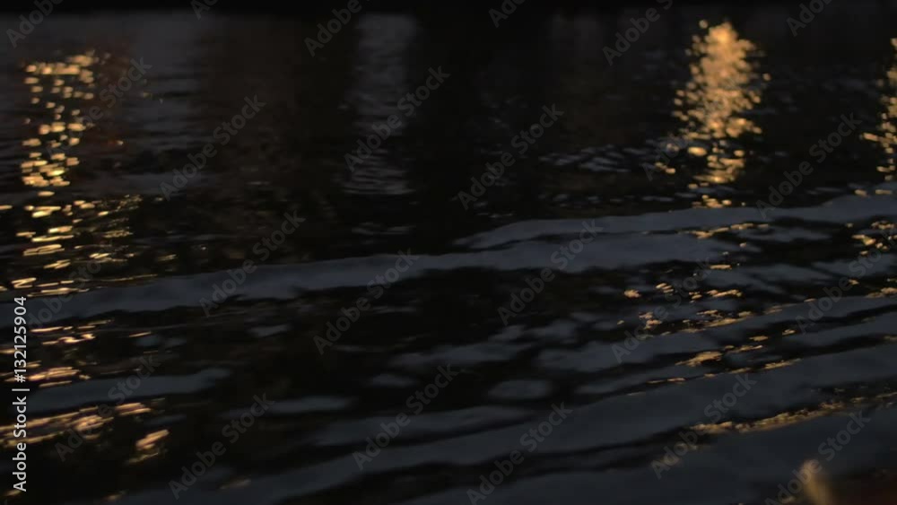 Close up view of river wave on moving boat at night, then buildings, cars on the waterfront, Amsterdam, Netherlands Close up view of river wave on moving boat at night, then buildings, cars on the waterfront, Amsterdam, Netherlands