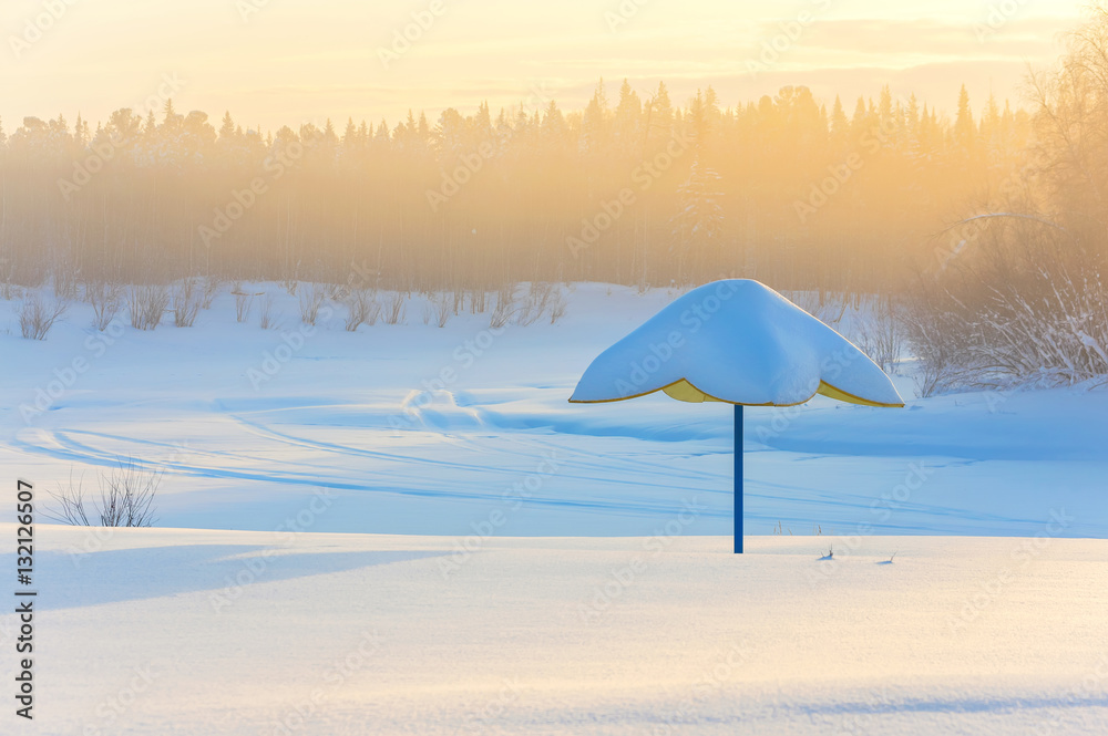 Beach umbrella on the bank of the frozen river. Foggy frosty morning.