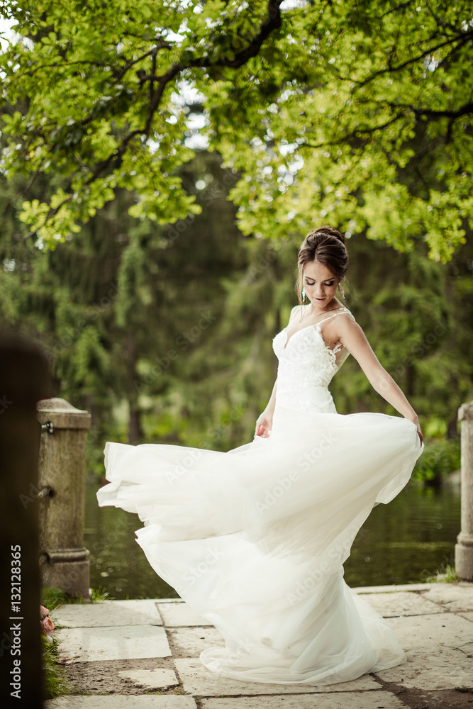 Bride spinning in a white dress on the bank of the lake in the sunset sun