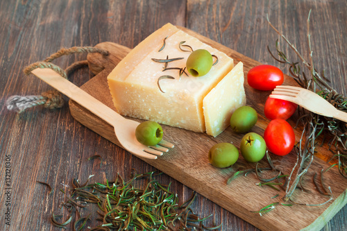 Parmesan cheese, green olives, rosemary, red cherry tomatoes on wooden table. Closeup.