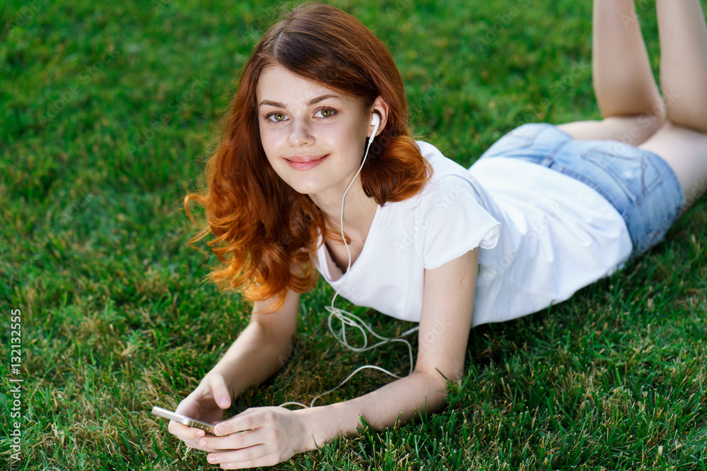Fototapeta premium beautiful young woman in a light t-shirt, relaxing on the grass in a park, trees, nature