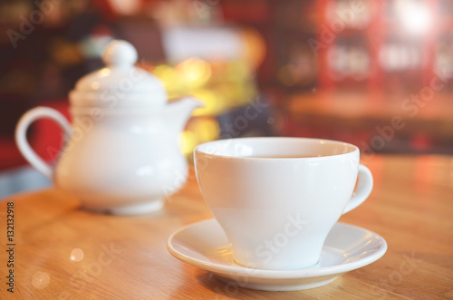 Cup of hot tea with a white pot on a wooden table