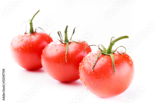 Three ripe tomatoes with green stems and water droplets in a diagonal line on a white background
