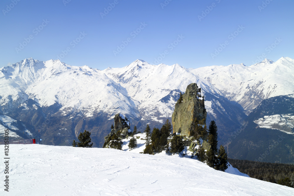 Rock surrounded by pine trees on a skiing slope on the background of alpine peaks in French Alps, Les Arcs, Paradiski