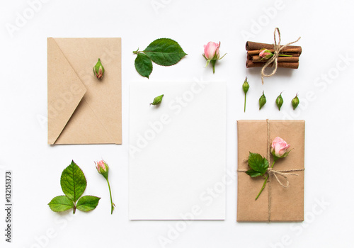 Letter, envelope and gift on white background. Invitation cards, or love letter with pink roses. Holiday concept, top view, flat lay
